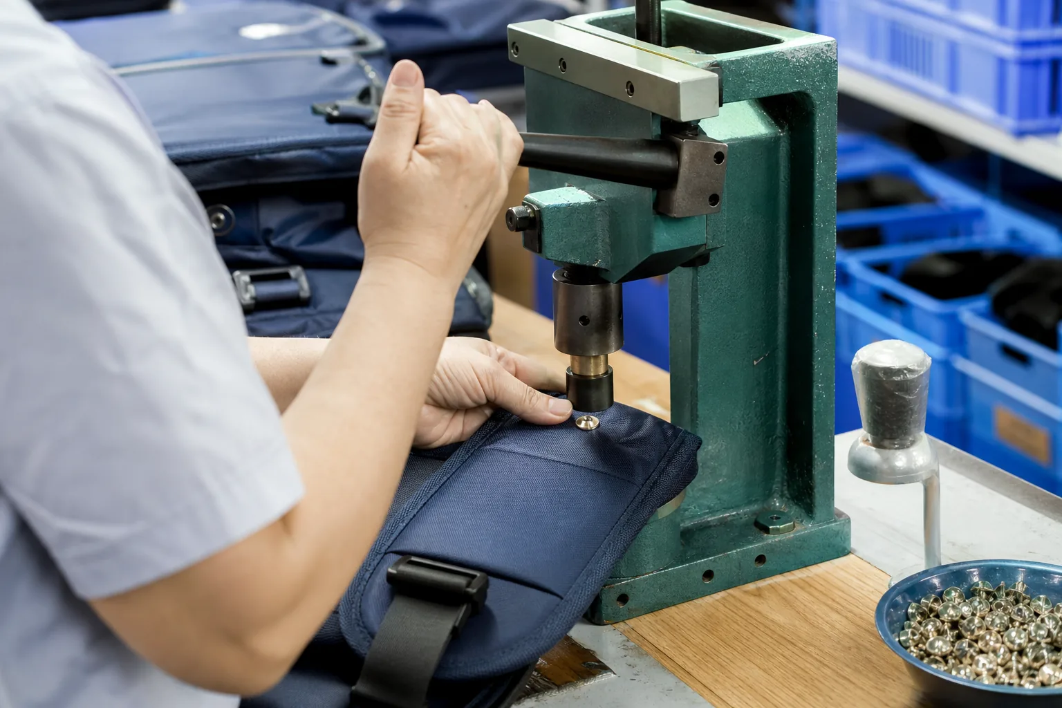 Operator setting a metal snap fastener onto a backpack flap with a hand press