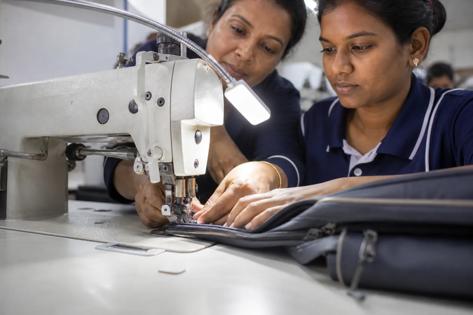 A trainer guiding a trainee's hands on fabric through a heavy-duty walking foot machine